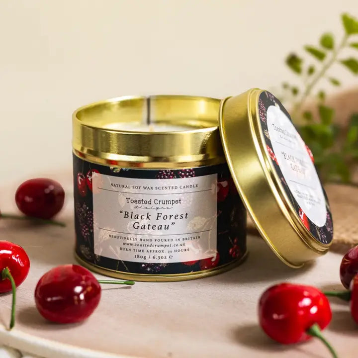 Scented candle in a tin with a label, surrounded by cherries on a wooden surface.