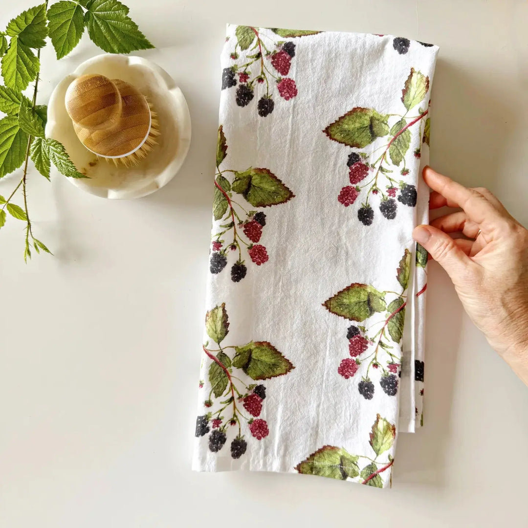 Hand holding a floral-patterned towel with berries and leaves on a white surface.
