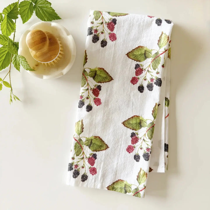 Tea towel with berry and leaf pattern next to a teacup on a white surface