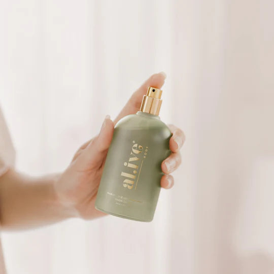 Hand holding a green bottle with gold cap against a light background