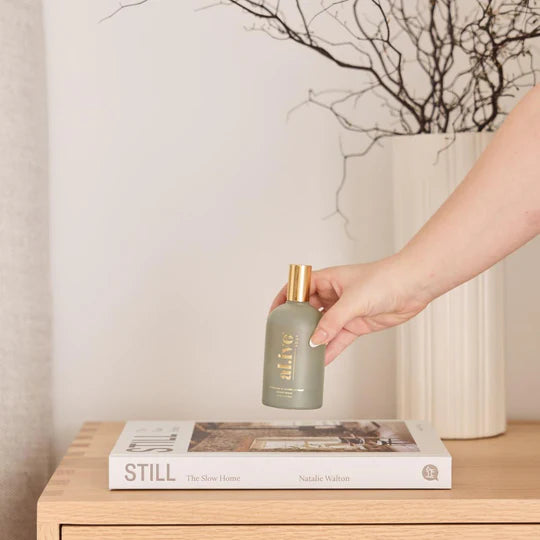 Hand holding a bottle labeled 'alive' on a wooden surface with a book and decorative elements.
