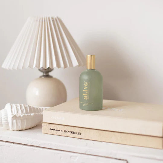 Green bottle labeled 'alive' on a stack of books with a lamp in the background