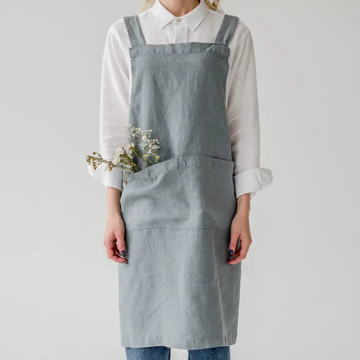 Person wearing a gray apron over a white shirt on a plain background