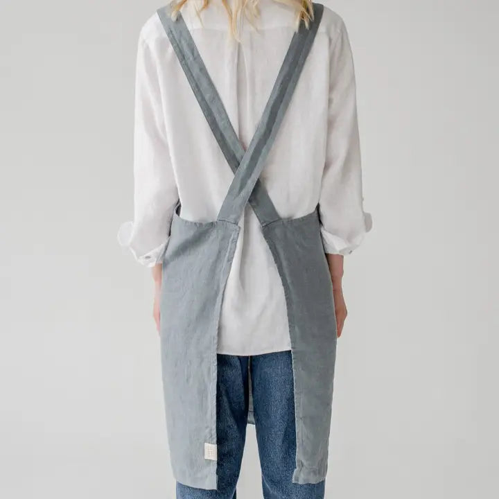 Person wearing a light gray apron over a white shirt and blue jeans on a plain background