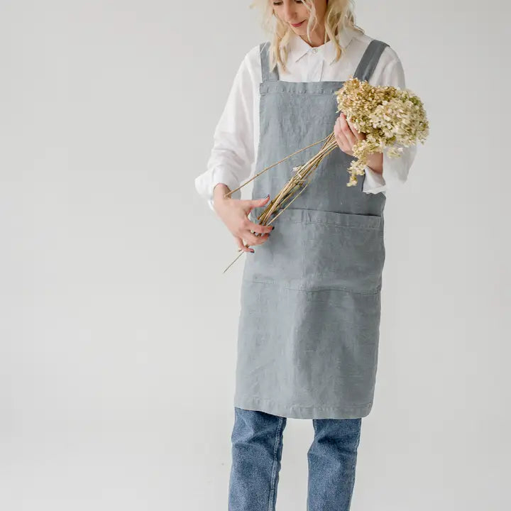 Person wearing a light blue apron holding a bouquet of flowers against a plain background