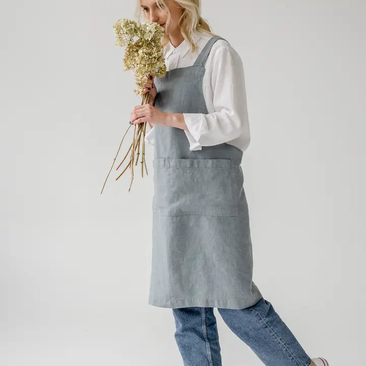 Person wearing a light blue apron holding a bouquet of flowers on a plain background