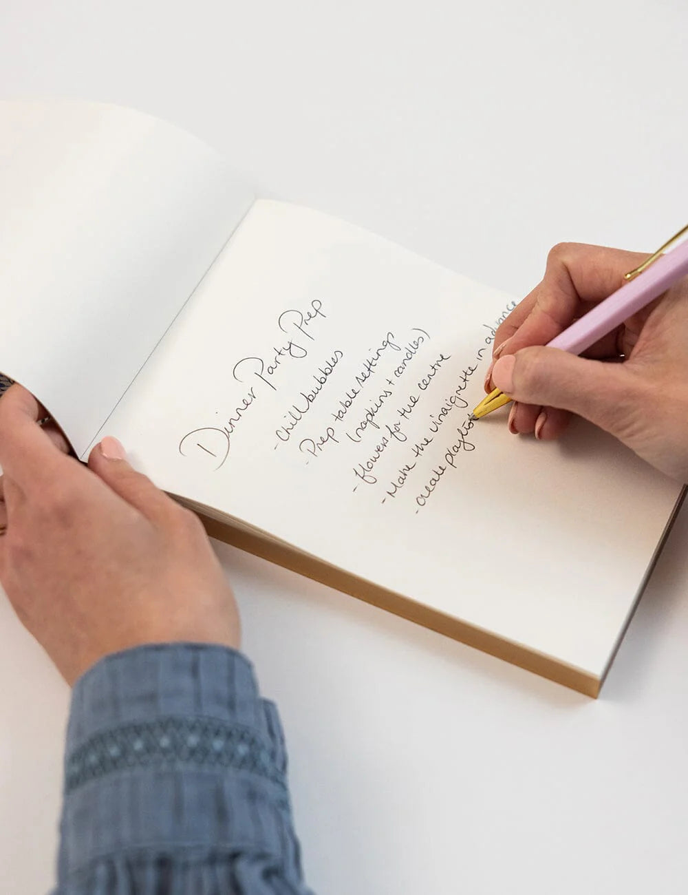 Person writing in a notebook with a pen on a white surface