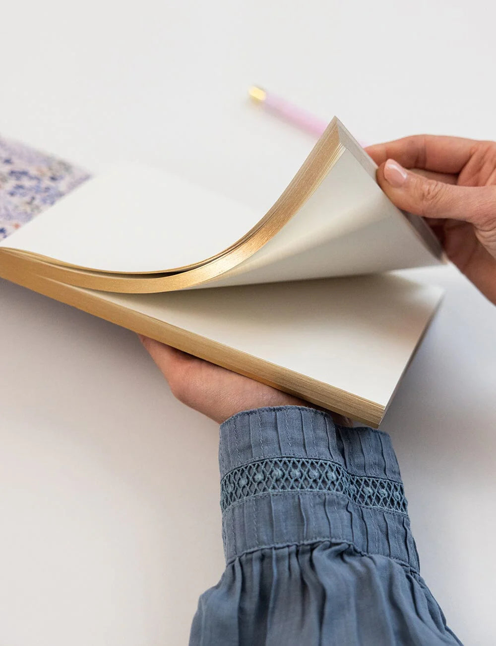 Person holding an open book with a pink pen on a light background