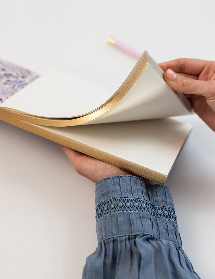 Person holding an open book with a pink pen on a light background