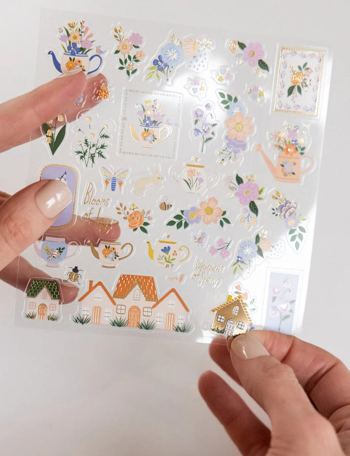 Sheet of decorative stickers featuring houses, flowers, and other elements held by a person.
