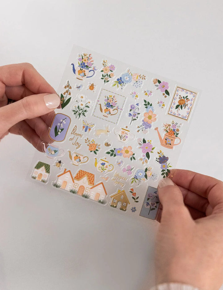 Hand holding a sheet of decorative stickers with floral and nature-themed designs on a white background.