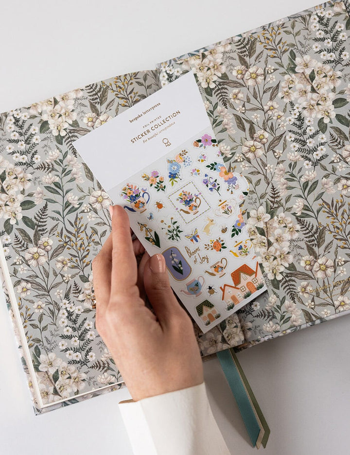 Hand holding a sticker book with floral stickers over a floral-patterned notebook