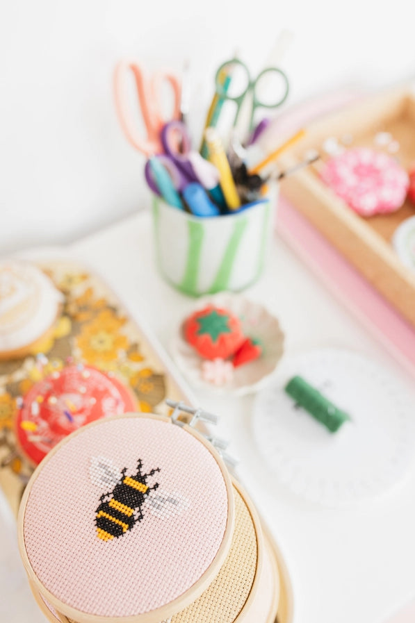 Cross-stitched bee on a wooden hoop with embroidery supplies in the background