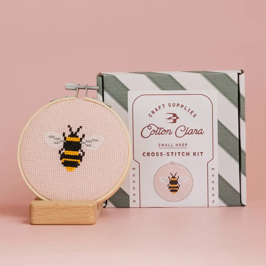 Cross-stitch kit with a bee design and Cotton Clara packaging on a pink background