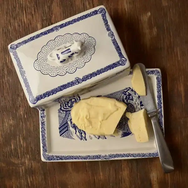 Butter dish with blue decorative border containing a stick of butter and a knife on a wooden surface.