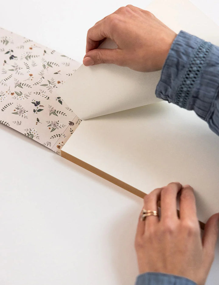 Person opening a notebook with floral patterns on a white surface