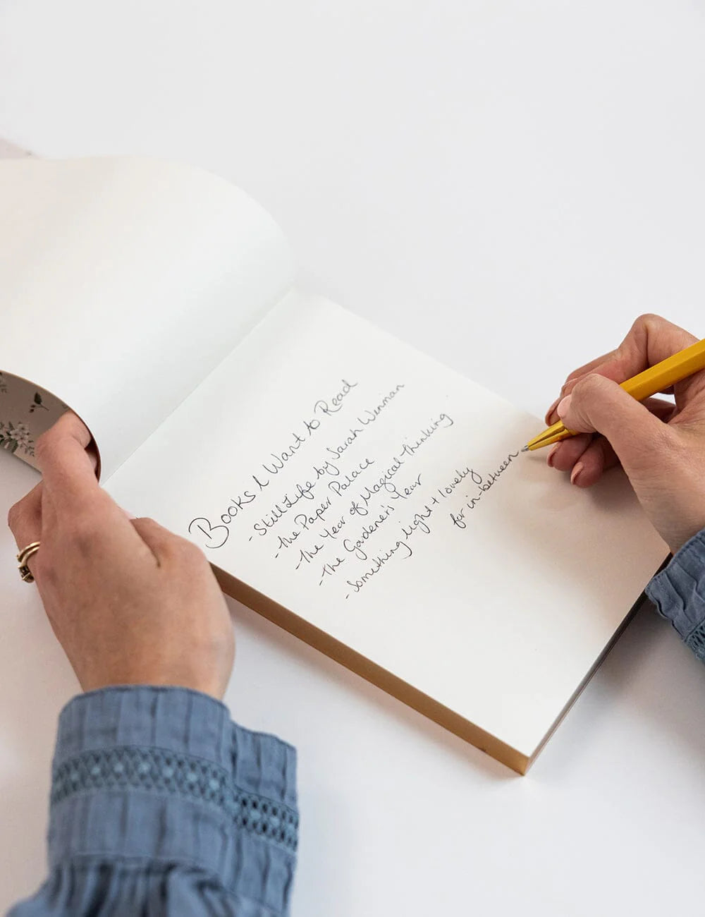 Person writing in a notebook with a yellow pen on a white background