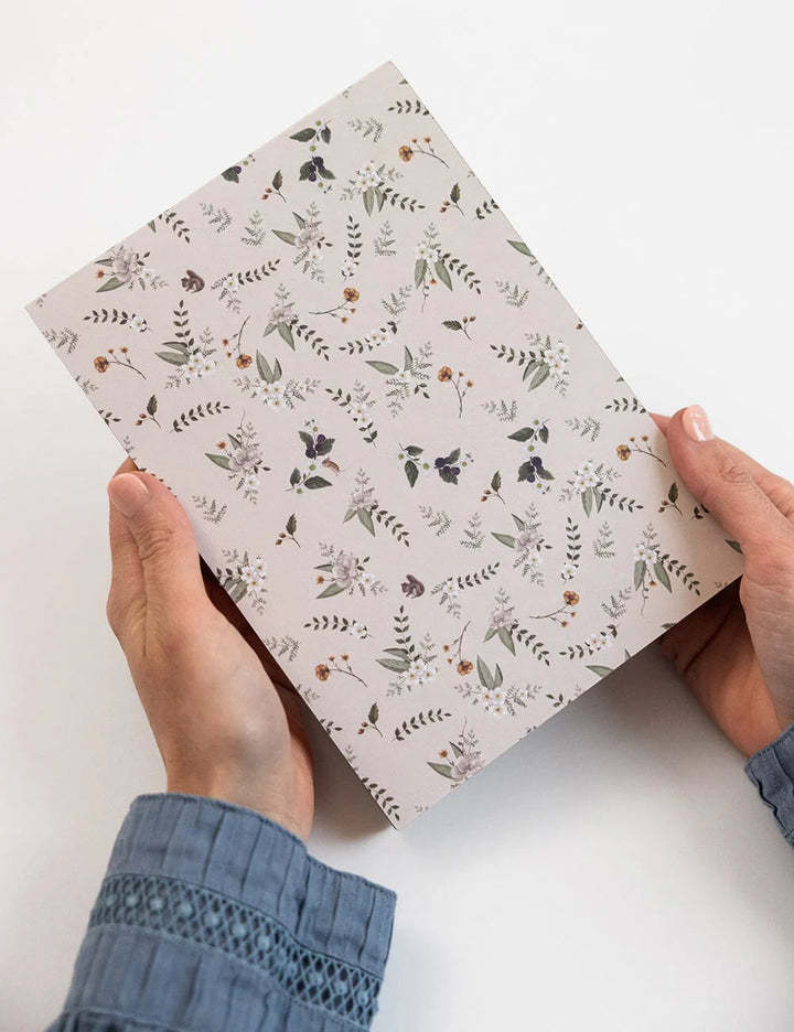 Person holding a notebook with floral pattern on a white background