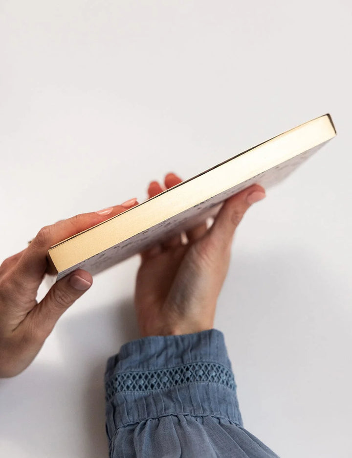 Person holding a gold and white rectangular notepad against a white background