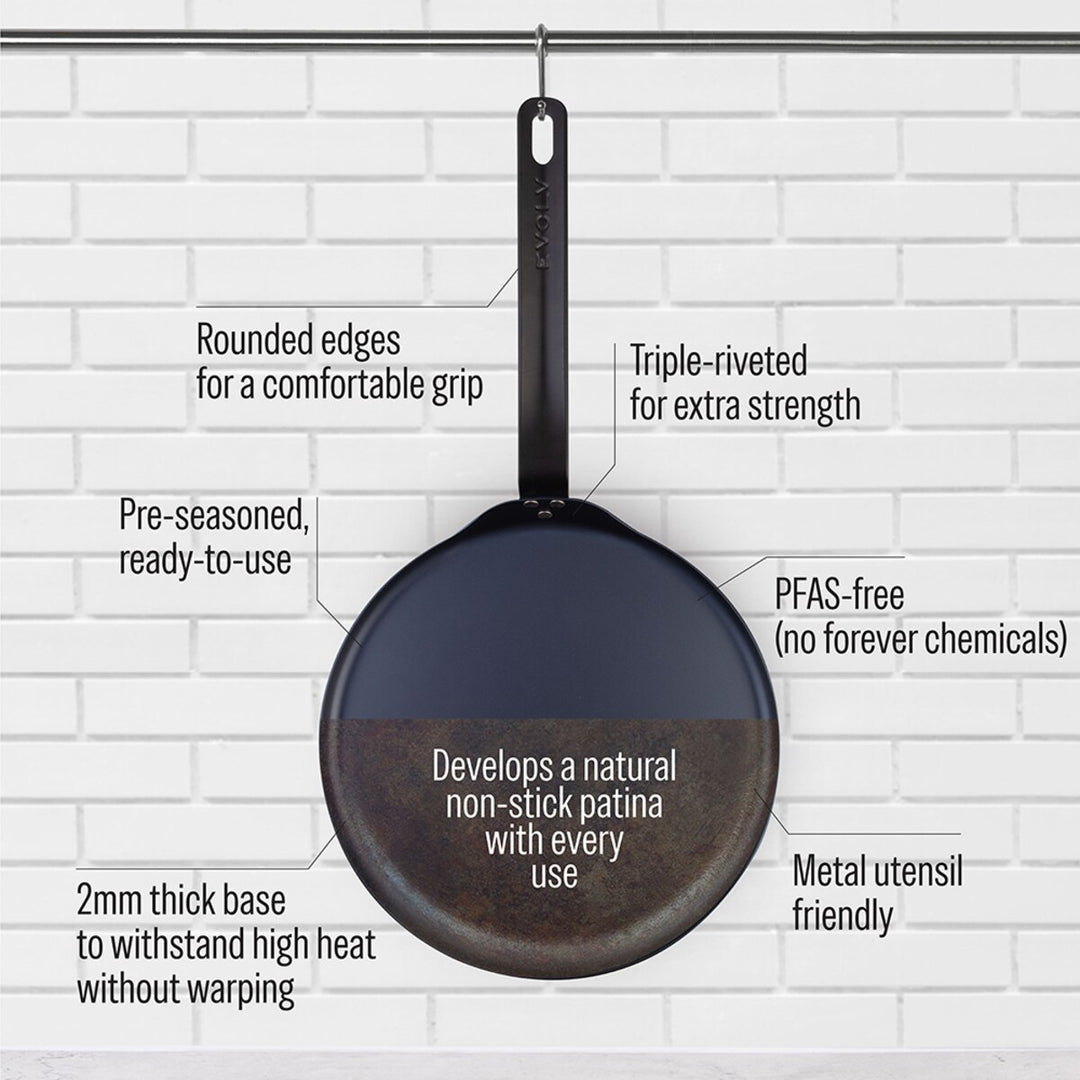 Black carbon steel pancake pan with text highlighting features on a white brick wall background