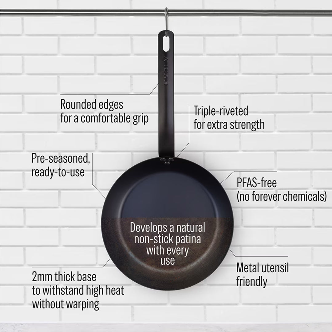 Black carbon steel frying pan with text highlighting features on a white brick wall background