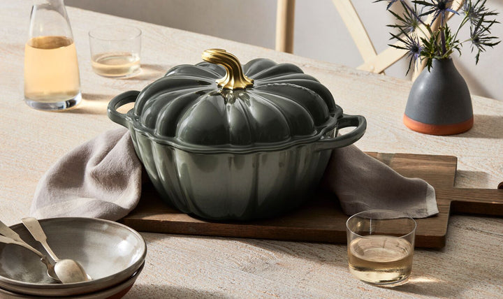 Green ceramic pot on a wooden table with glasses and a vase in the background