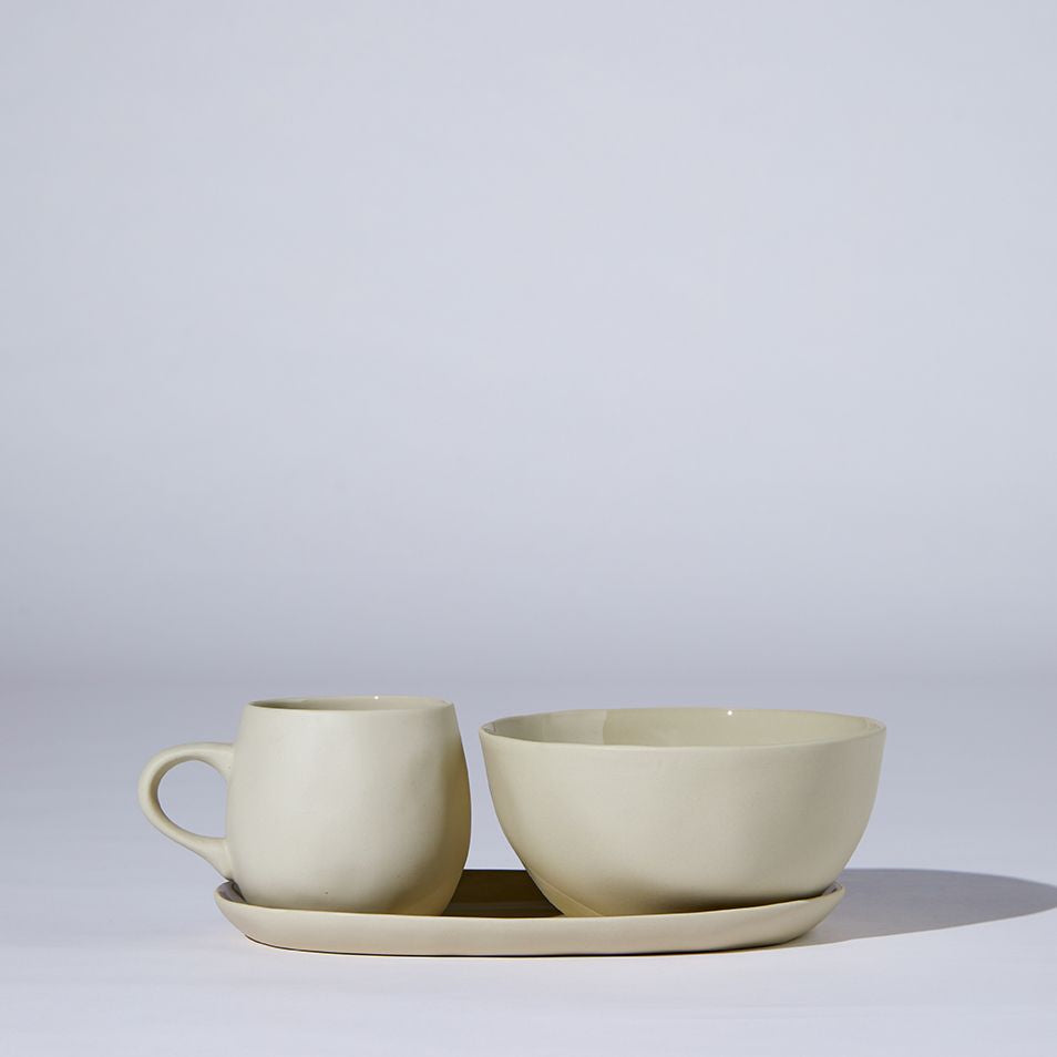 Beige ceramic cup, bowl, and saucer set on a light gray background