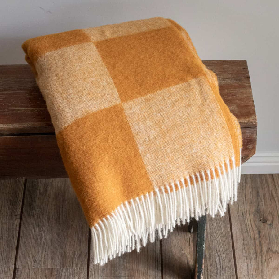 Checkered orange and beige blanket with white fringe on a wooden bench.