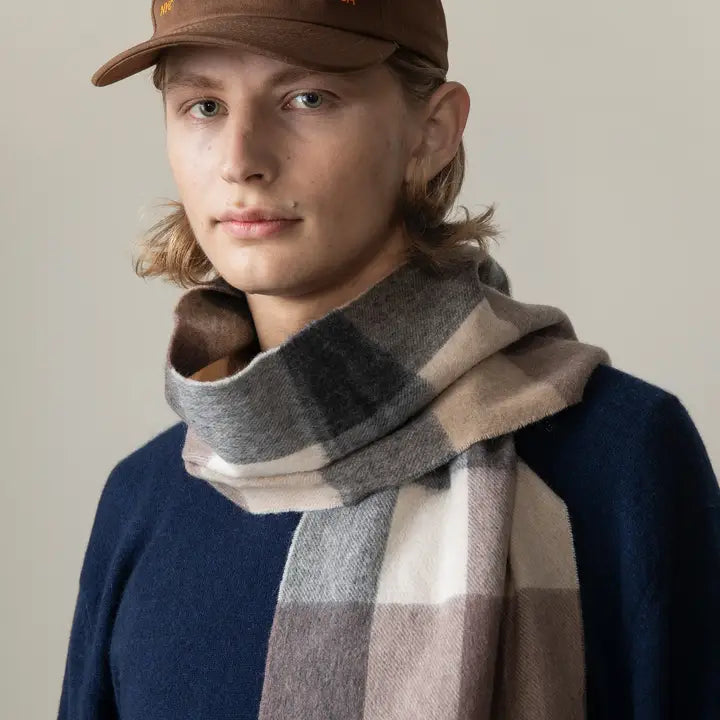 Person wearing a checkered scarf and brown cap against a neutral background