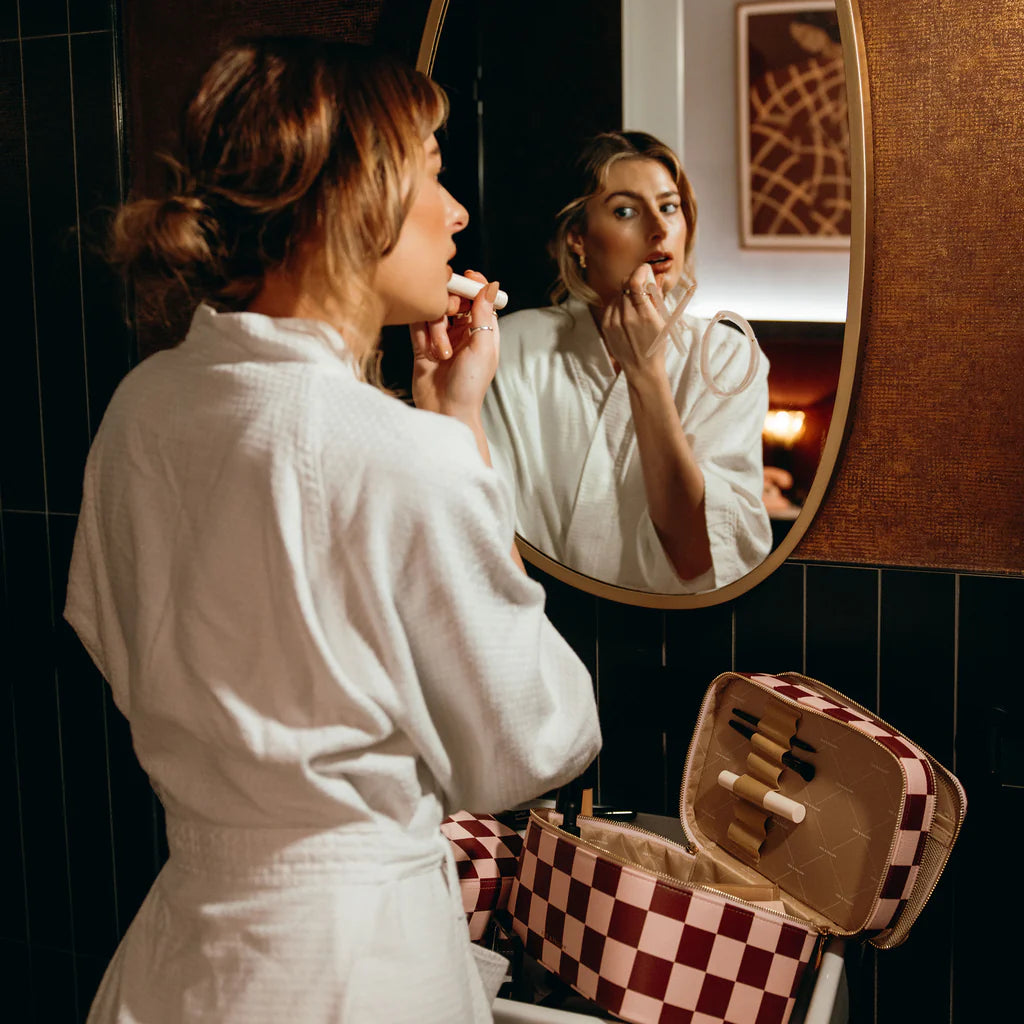 Woman applying makeup in front of a mirror in a bathroom.