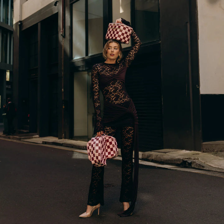 Woman in a patterned outfit holding checkered bags on a city street.
