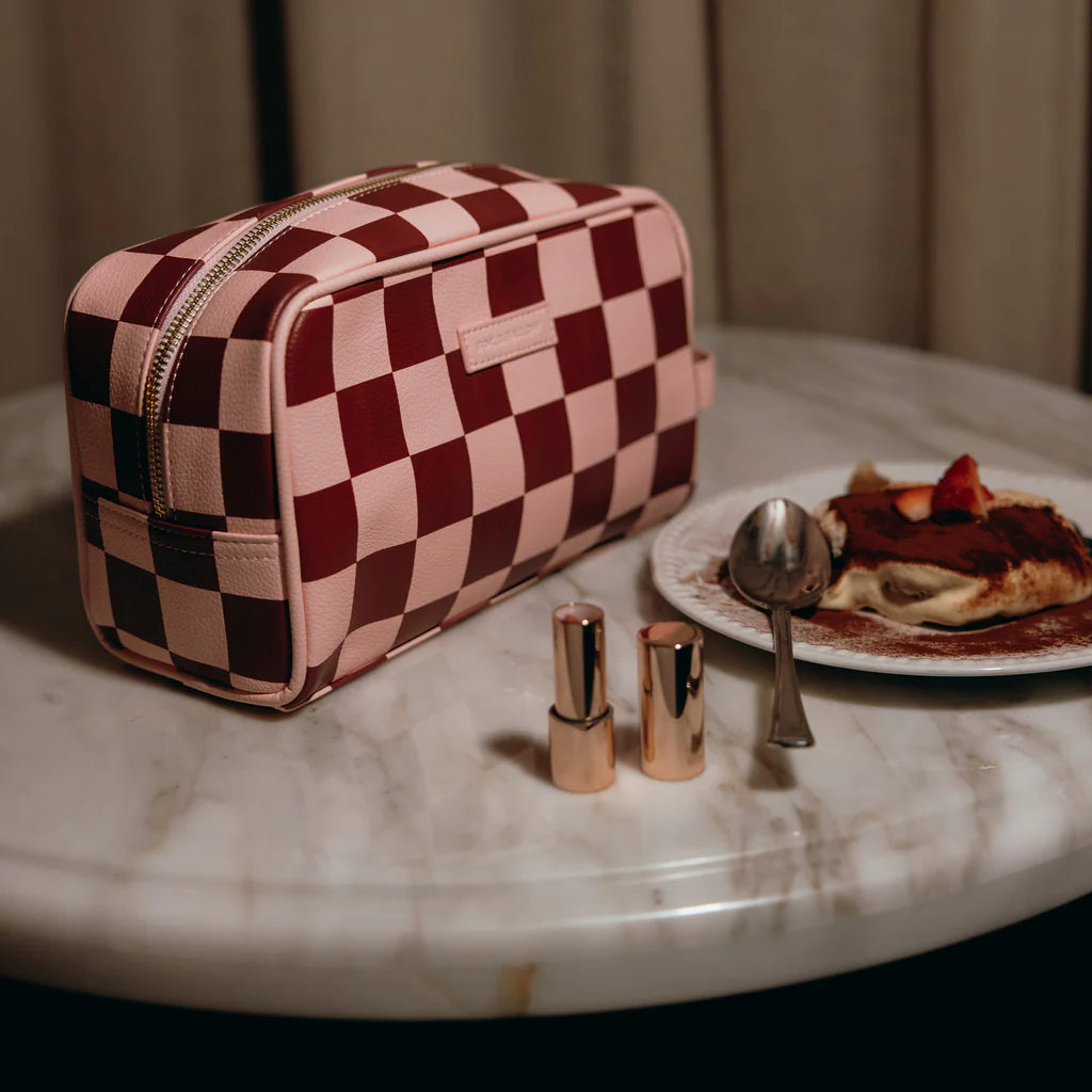 Checkered makeup bag on a marble surface with lipsticks and a plate of food.