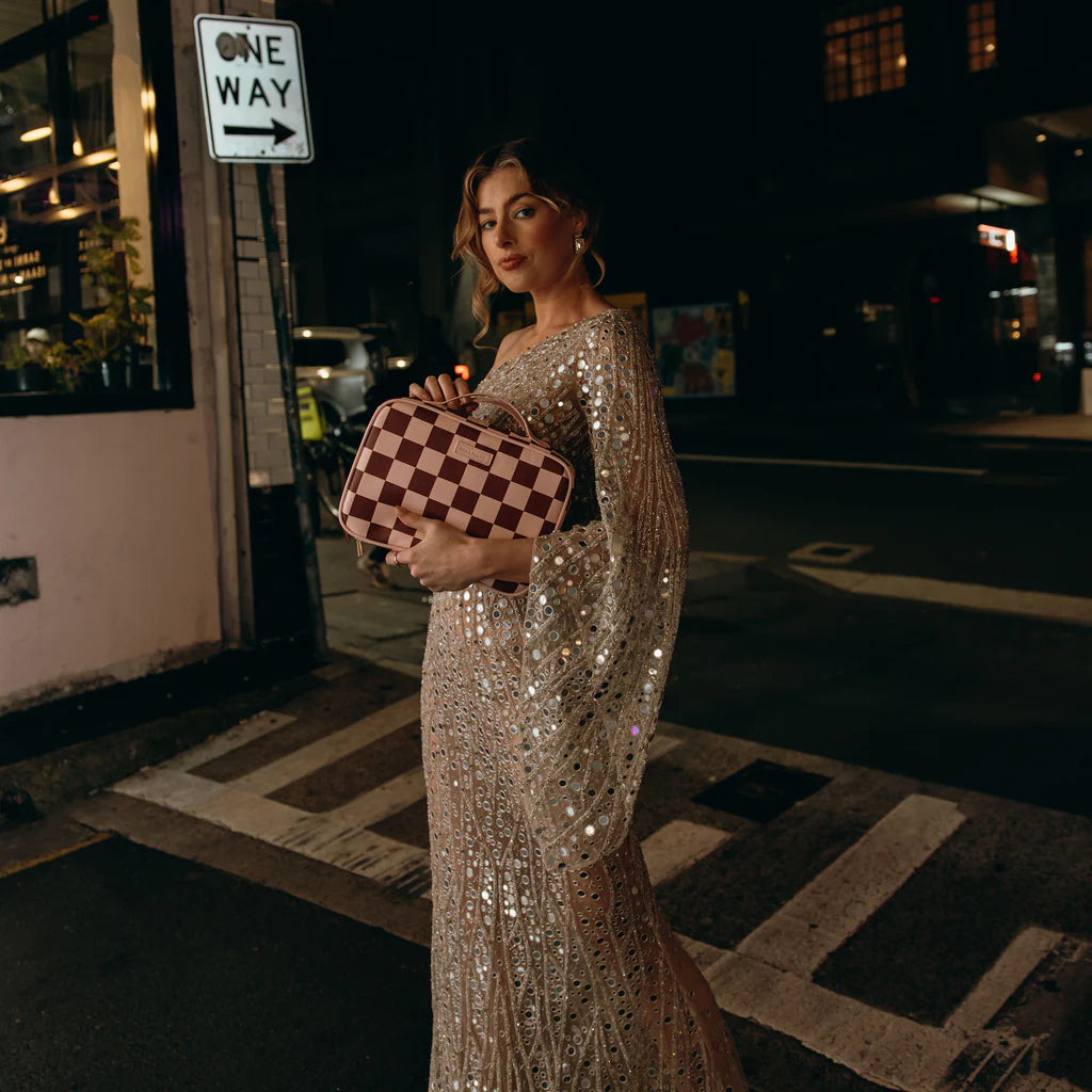 Woman in a sparkling silver dress holding a checkered cosmetic bag on a city street at night.