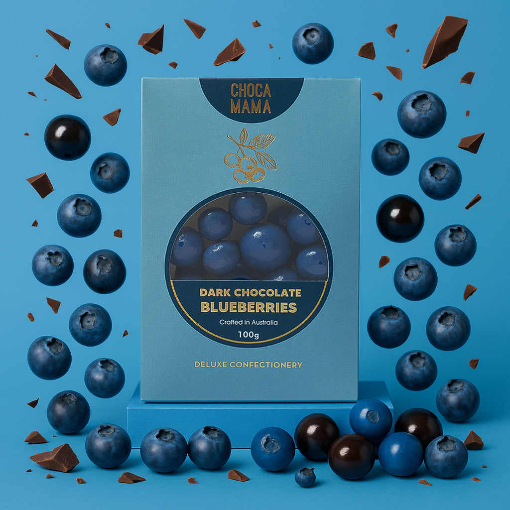 Box of Choco Mama Dark Chocolate Blueberries on a blue background with blueberries and chocolate pieces around.
