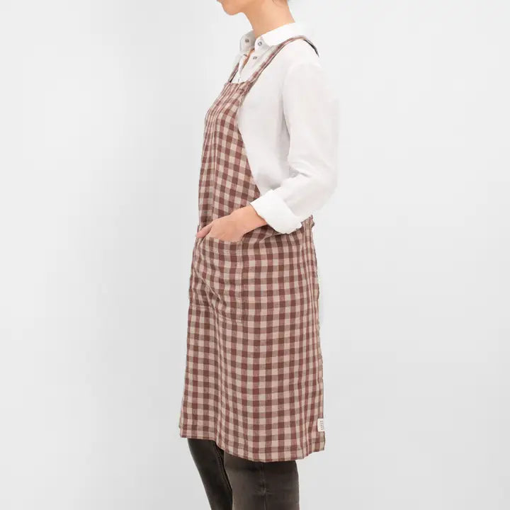 Person wearing a brown checkered apron over a white shirt on a light gray background