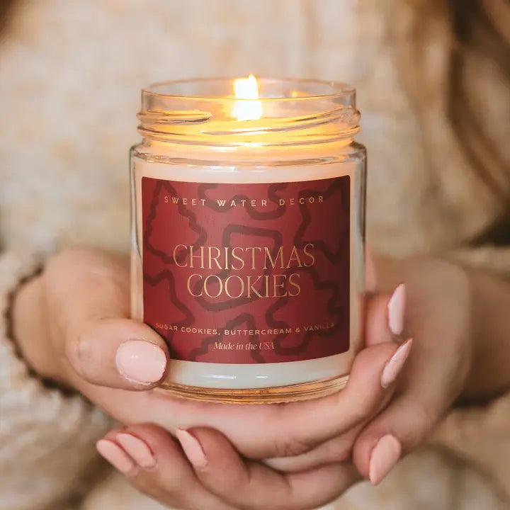 Candle labeled 'Christmas Cookies' held by a person with a blurred background