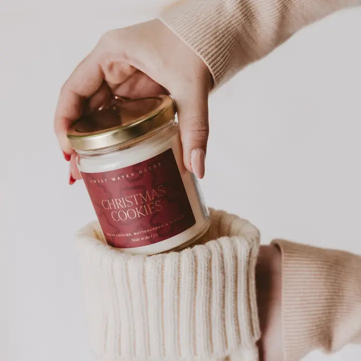 Hand holding a 'Christmas Cookies' scented candle jar with a gold lid.