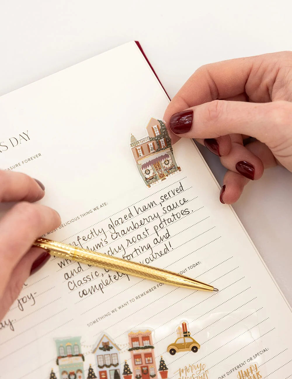 Person using a gold pen to write in a notebook with decorative stickers on a white surface