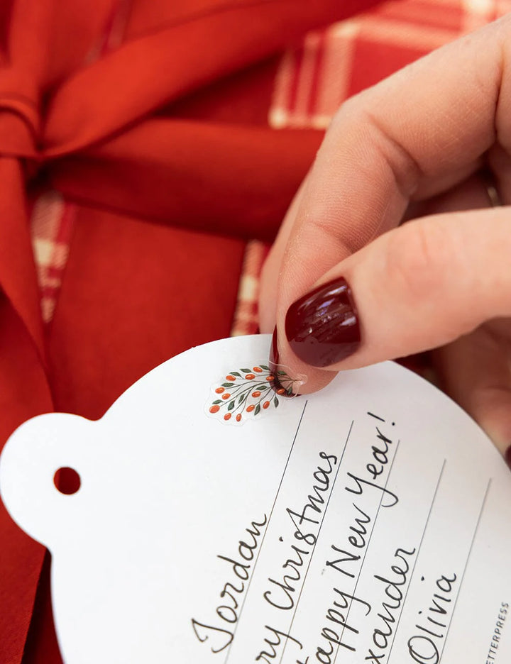 Hand holding a personalized Christmas gift tag with red fabric in the background