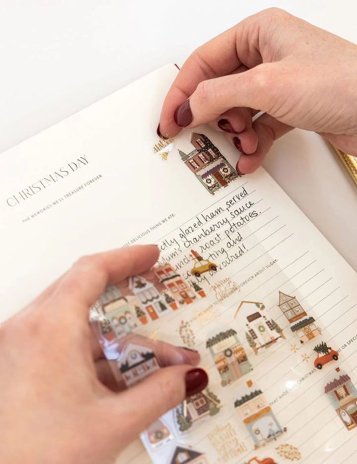 Person applying Christmas-themed stickers to a notebook page.