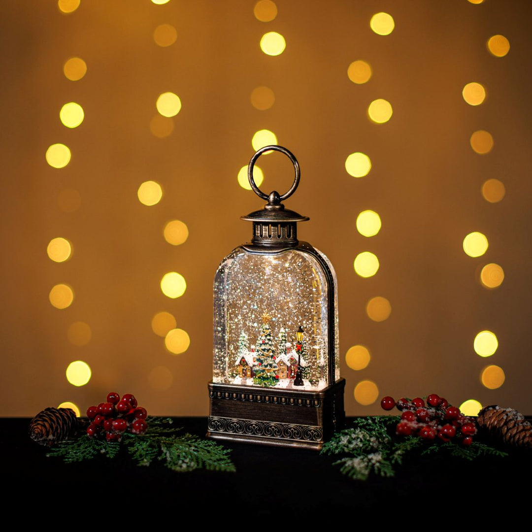 Decorative lantern with a Christmas scene inside, surrounded by festive decorations and lights on a warm background.
