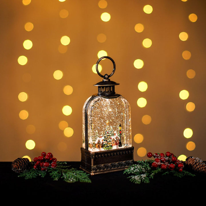 Decorative lantern with a Christmas scene inside, surrounded by festive decorations and lights on a blurred background.