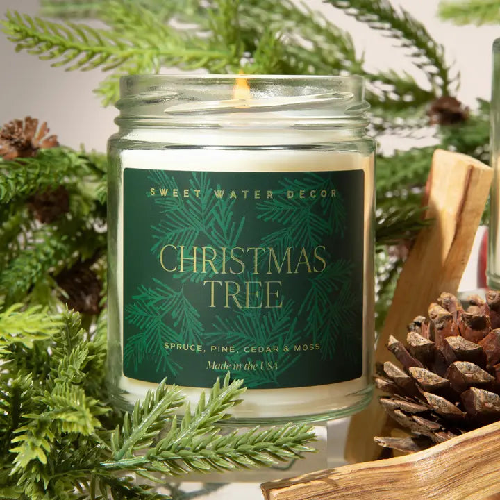 Candle in a jar labeled 'Christmas Tree' surrounded by greenery and pinecones