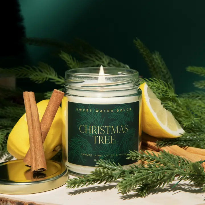 Candle labeled 'Christmas Tree' with cinnamon sticks, lemon slices, and greenery on a dark background