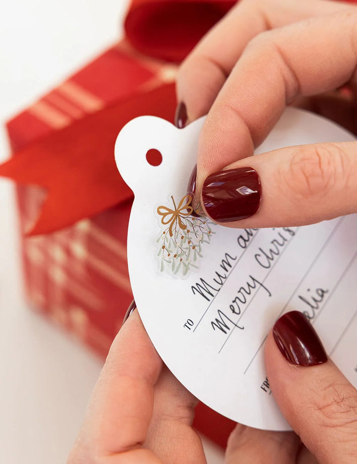 Hand holding a Christmas gift tag with red gift box in the background