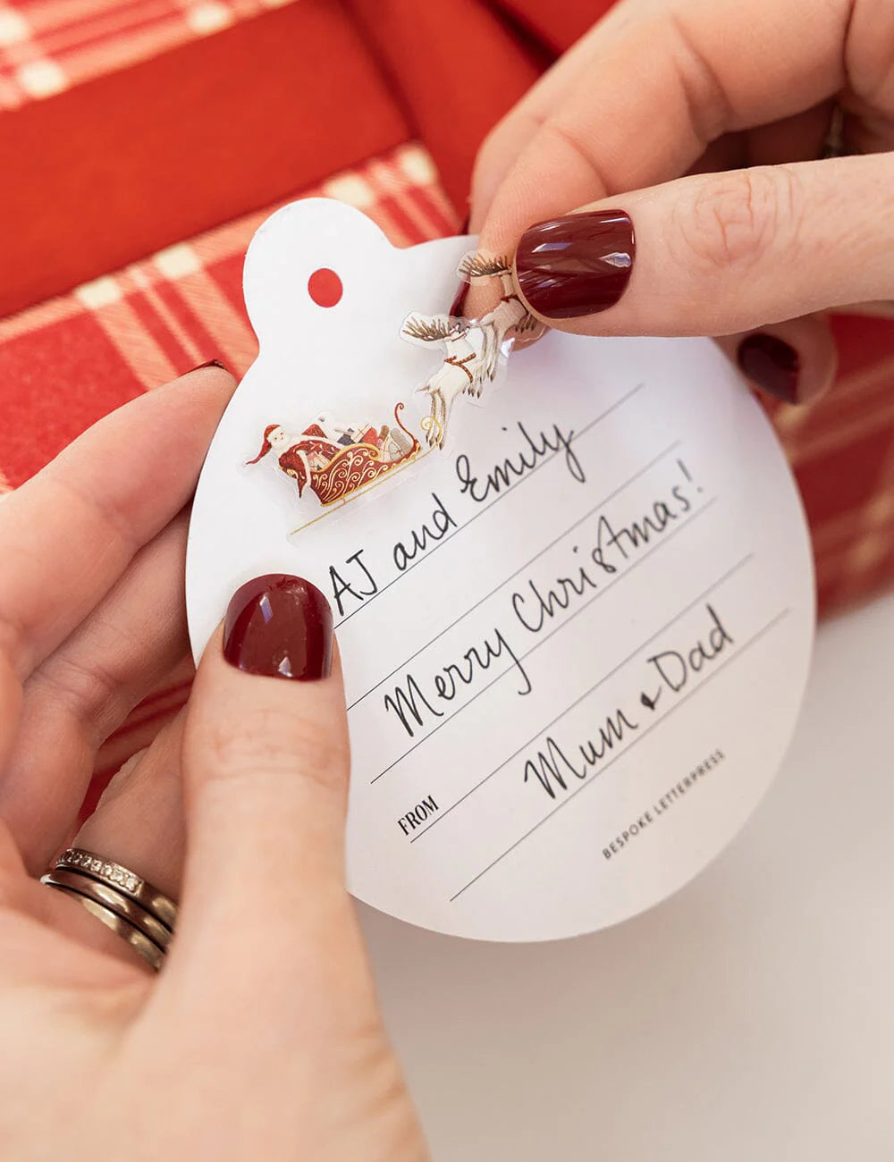 Hand holding a Christmas gift tag with personalized message against a red background