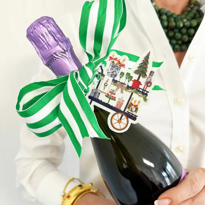 Bottle of champagne with a decorative ribbon and tag held by a person wearing a white coat.