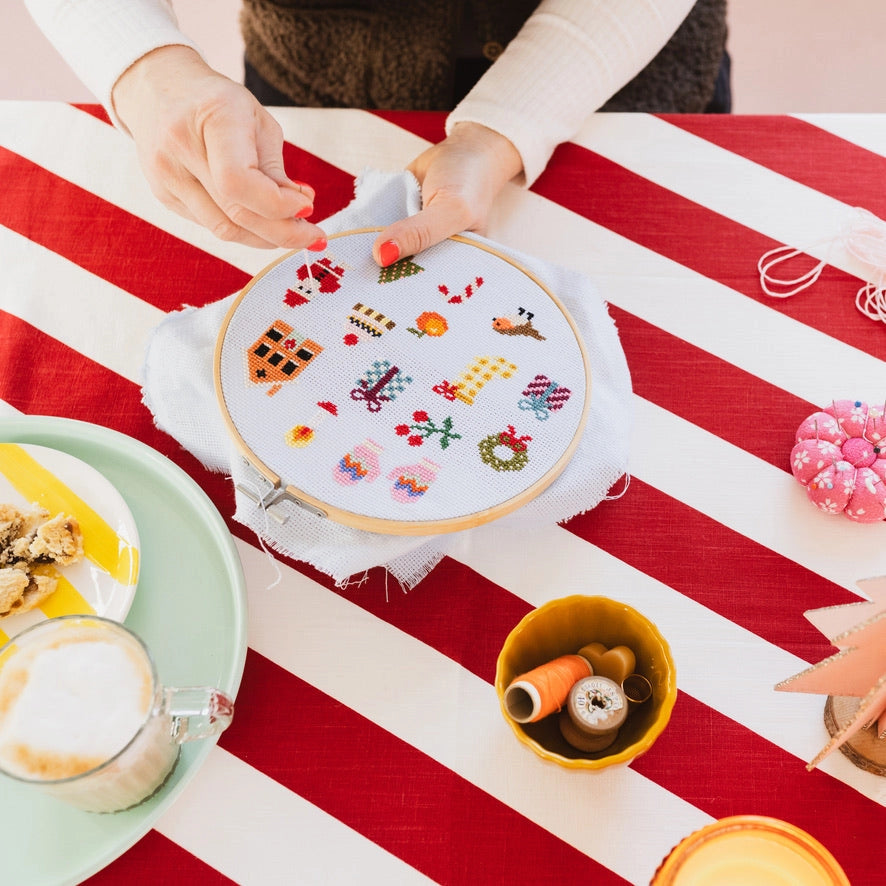 Person working on an embroidery hoop with colorful patterns on a red and white striped tablecloth.