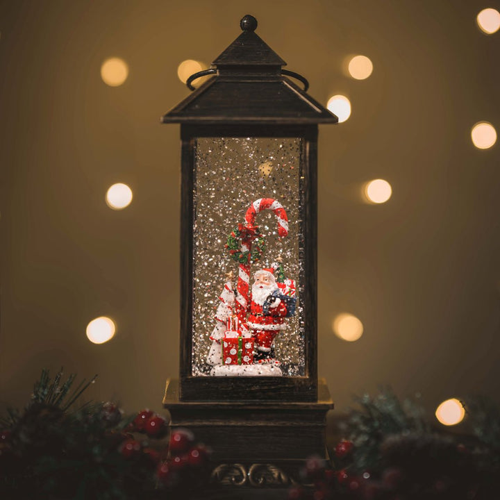 Decorative lantern with Santa Claus figure and candy cane against a warm, blurred light background