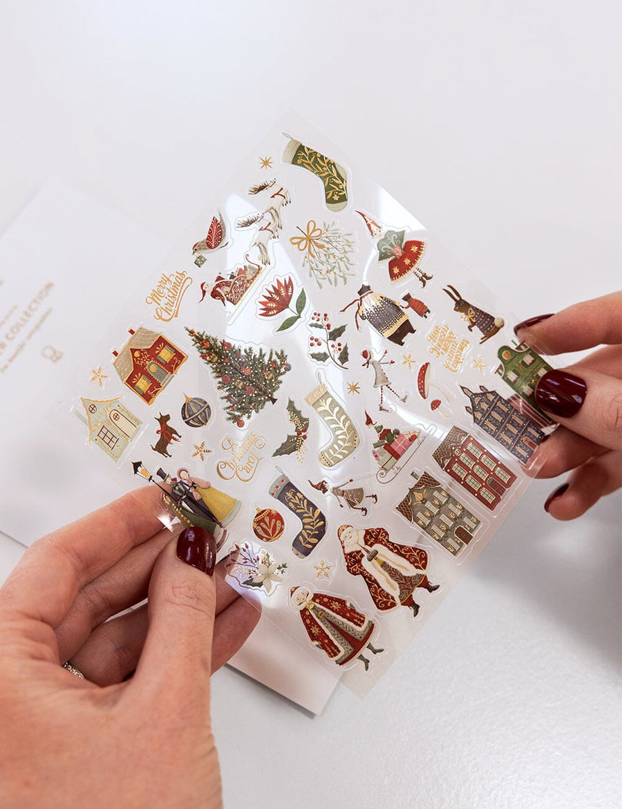 Sheet of decorative stickers with Christmas-themed designs held by a person.